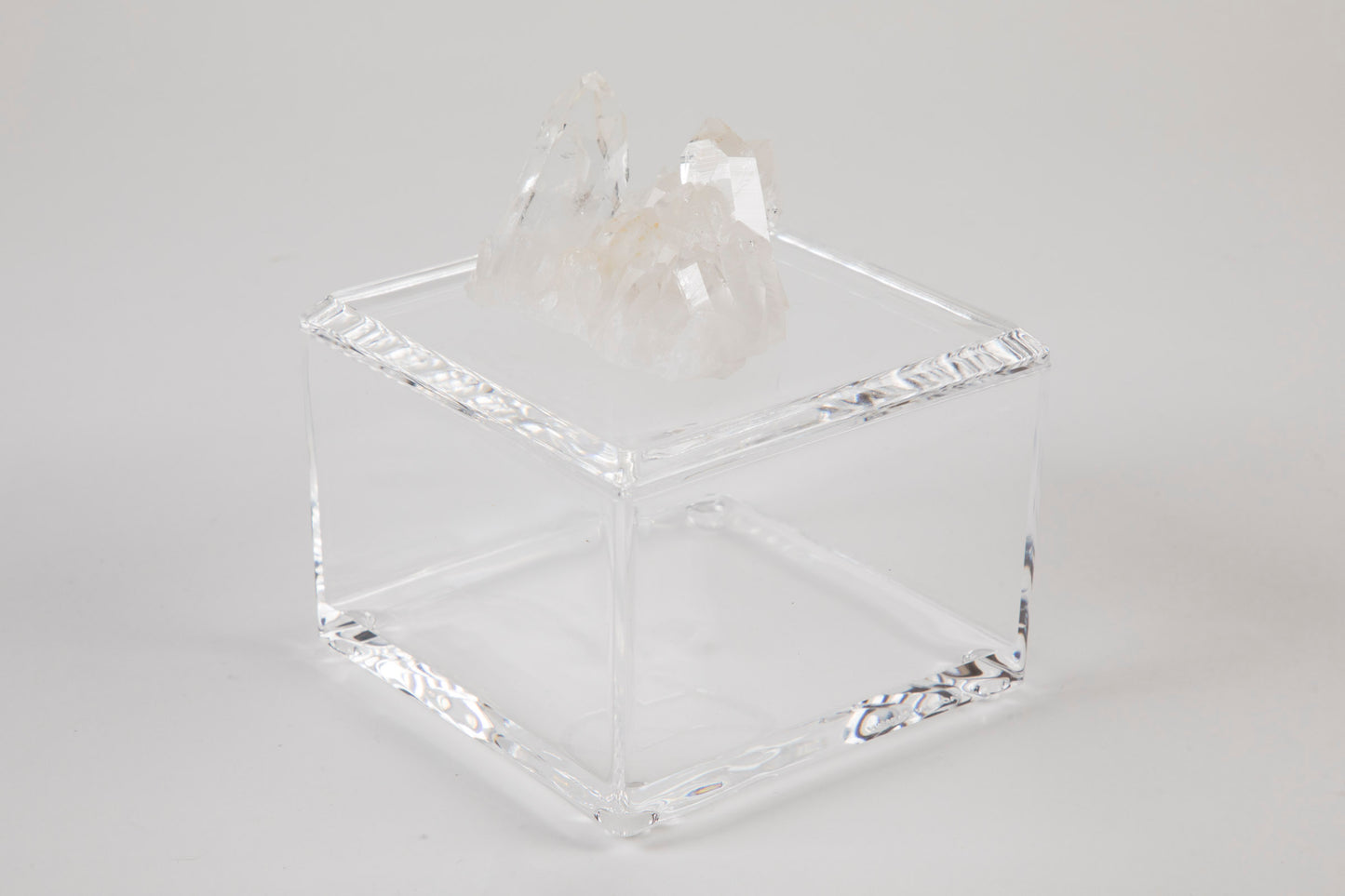 A clear acrylic square box with a removable lid, adorned with a white quartz crystal on top.