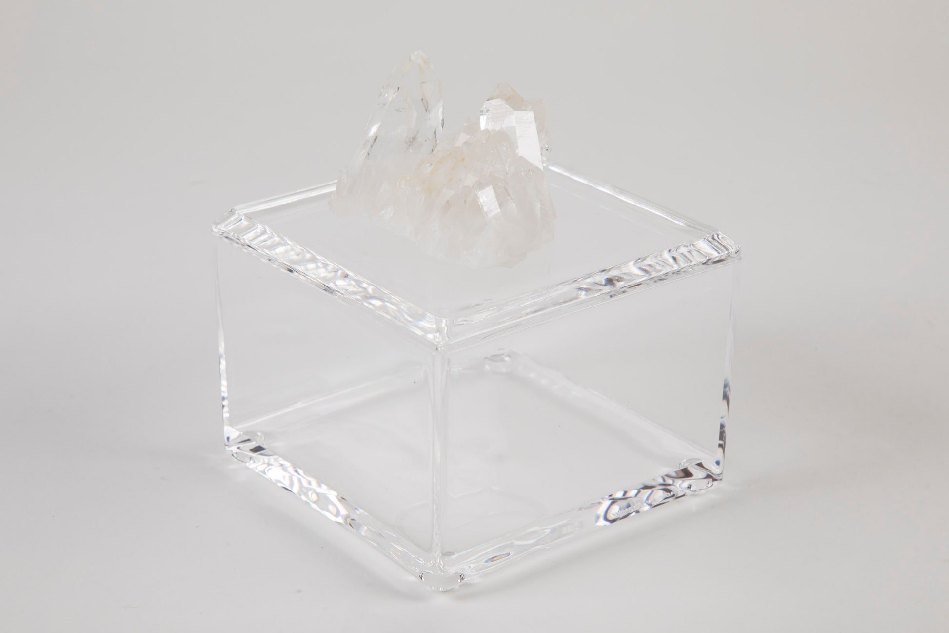 A clear acrylic square box with a removable lid, adorned with a white quartz crystal on top.