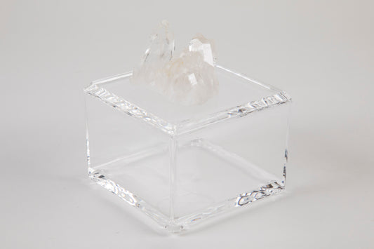 A clear acrylic square box with a removable lid, adorned with a white quartz crystal on top.