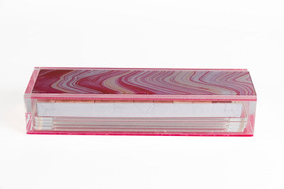 A clear acrylic case containing a set of tiles for a game, with visible pink accents on the edges of the case.