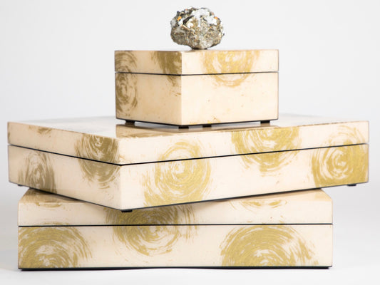 A set of lacquer boxes with a gold swirl pattern and a quartz topper, stacked with the largest box on top, adorned with a semi precious crystal.
