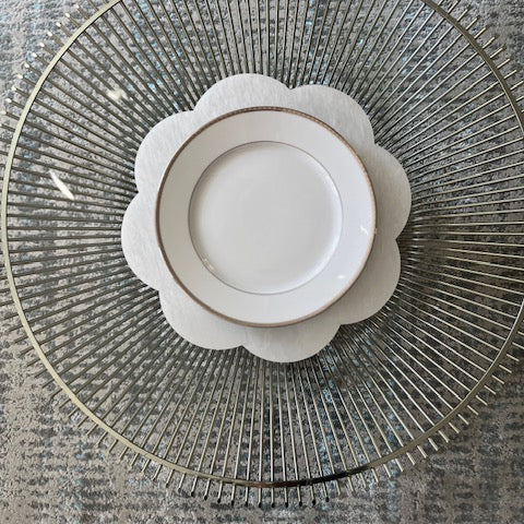 A scallop-edged acrylic placemat in a white marble pattern displayed with a white plate on top.