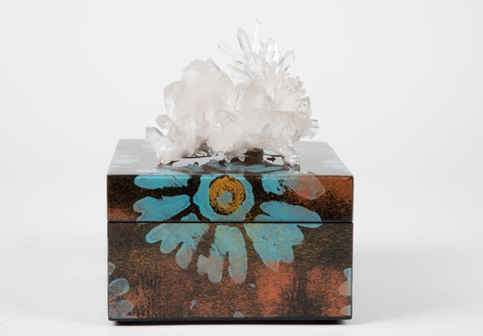 A decorative lacquer box with a semi precious crystal on the lid, featuring a floral pattern with blue and orange colors on a black background.